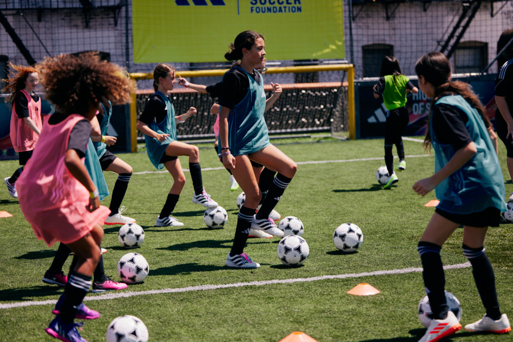 A group of girls in different color pinnies practice soccer footwork on a pitch